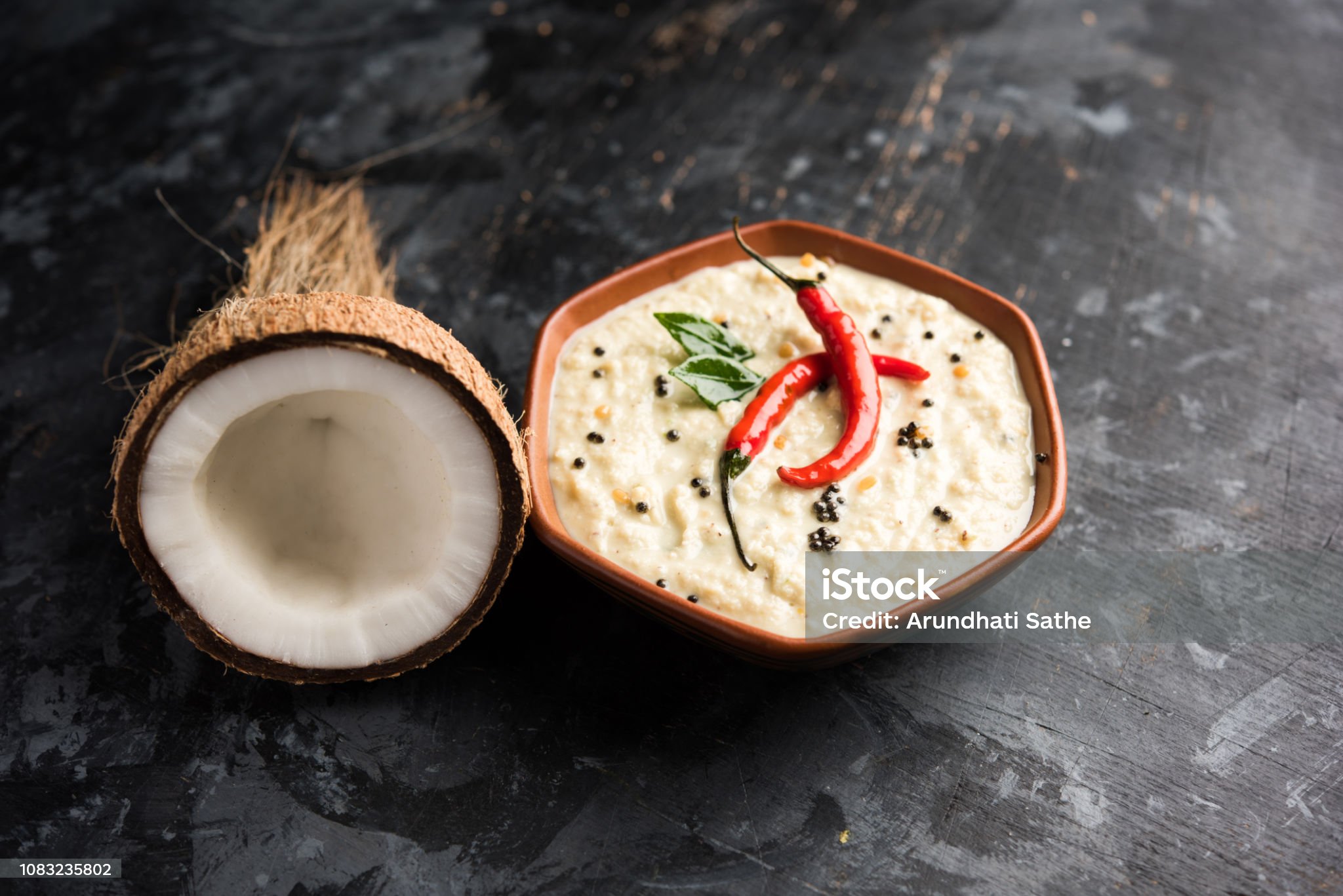 An image of delicious coconut chutney in a bowl and half a piece of coconut